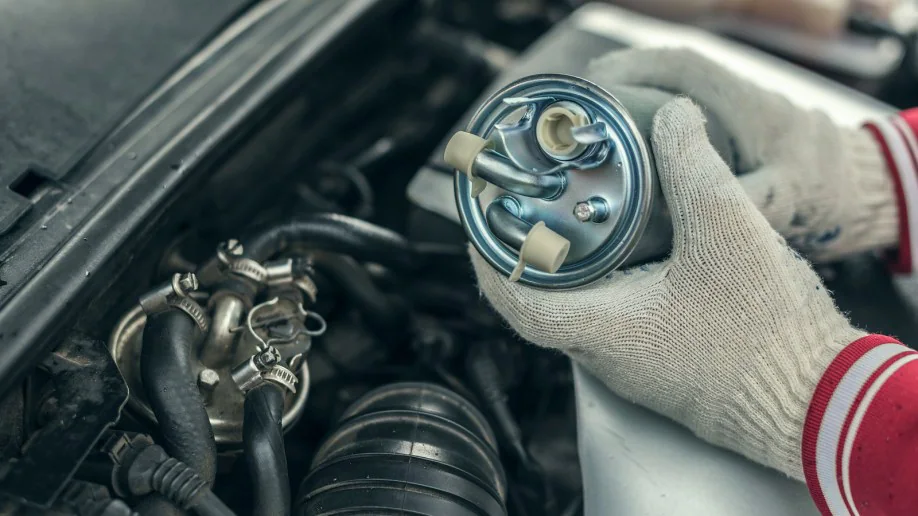 A mechanic in white gloves displays a fuel filter, emphasizing its importance in maintaining fuel quality, with an engine in the background.